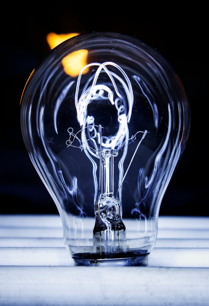 Artistic photo featuring a glowing light bulb with visible filament against a dark background.